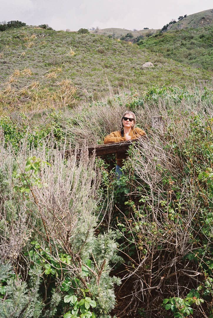 A woman in sunglasses leaning on a fence looking out twoards the camera