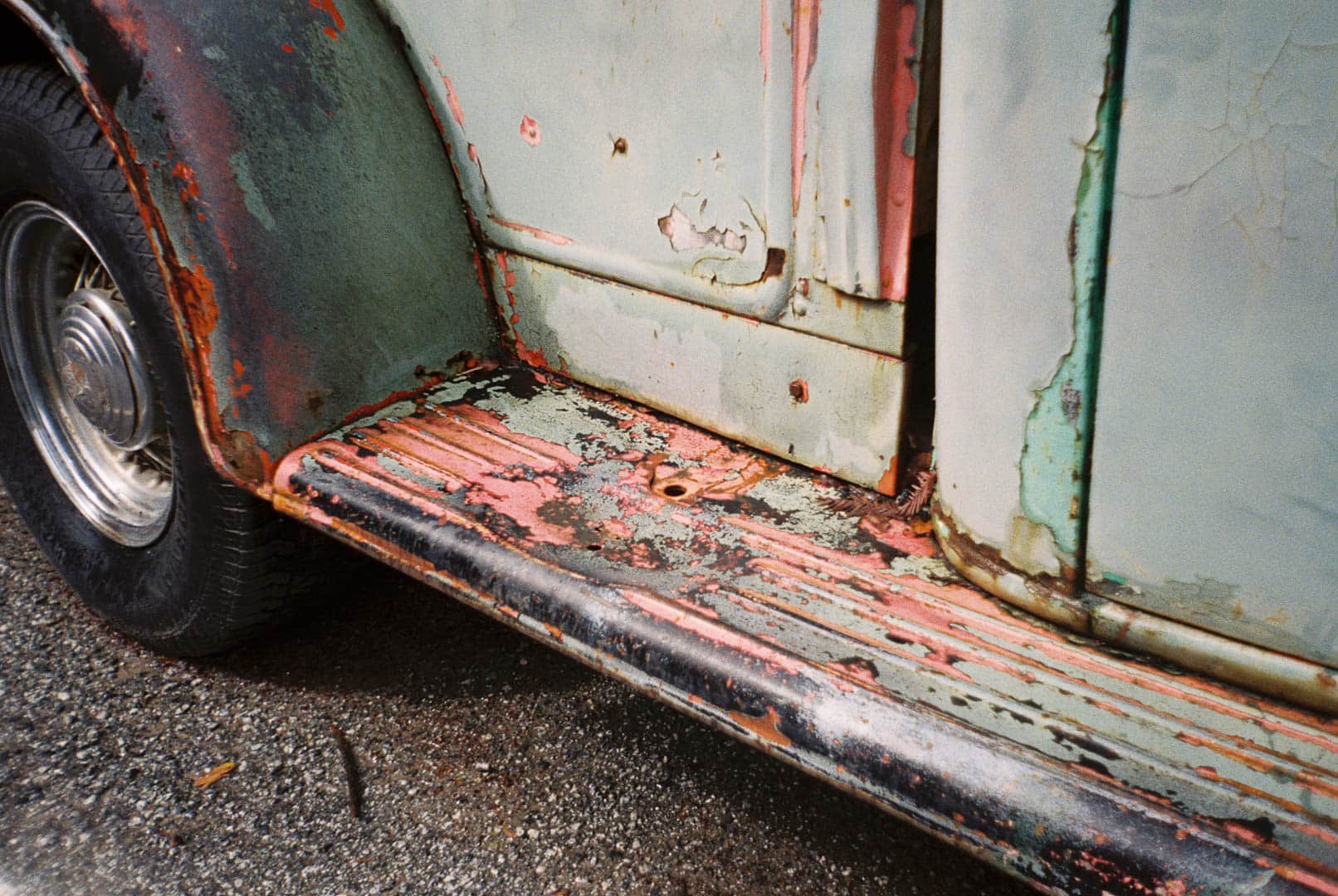 Old 1930s era Ford with weathered and pealing pale green paint in a light rain