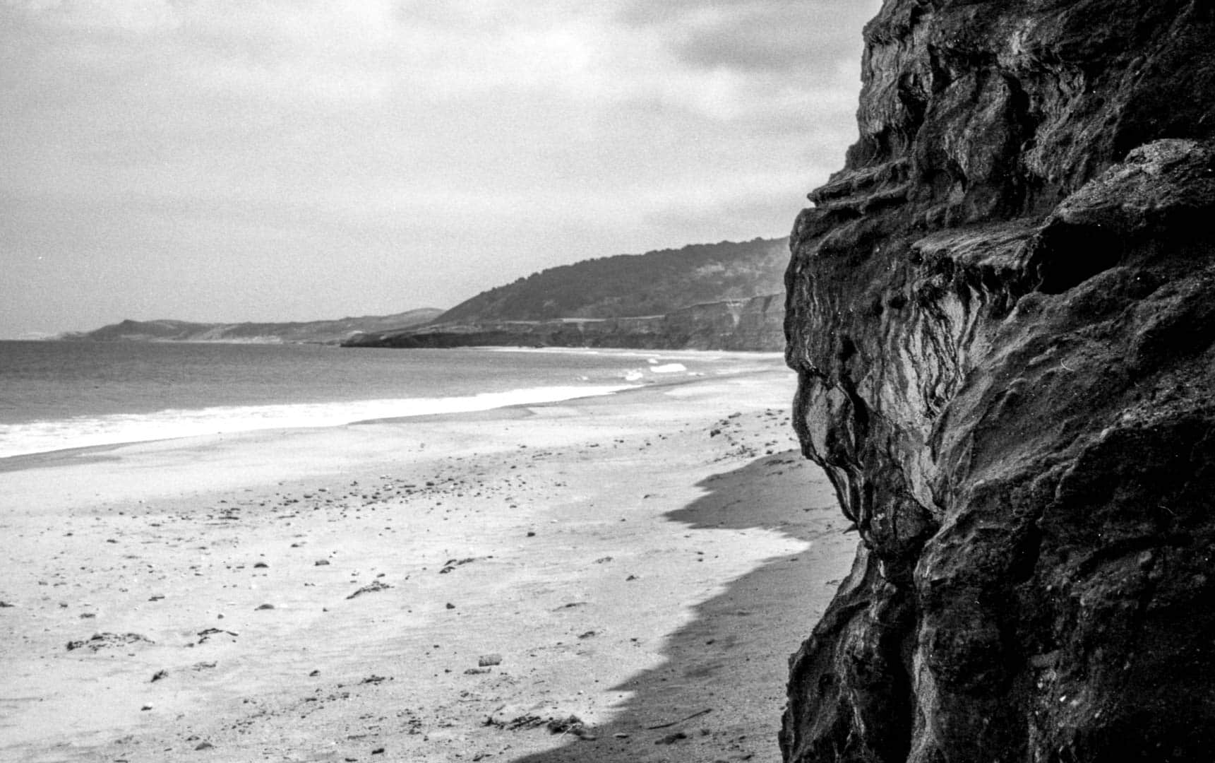 the dark jagged texture of a rocky bluff in the foreground with the windswept beach in the mid and background