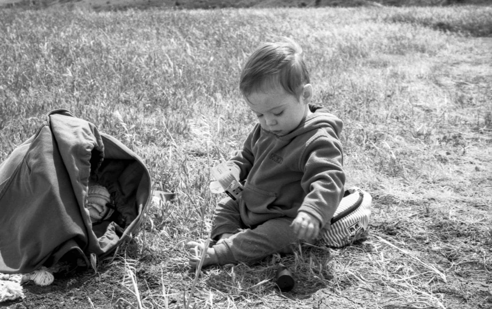 A baby playing in the grass next to a bag