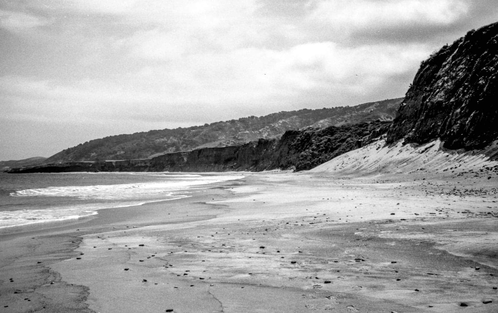 A sandy textured beach with dark rocky bluffs