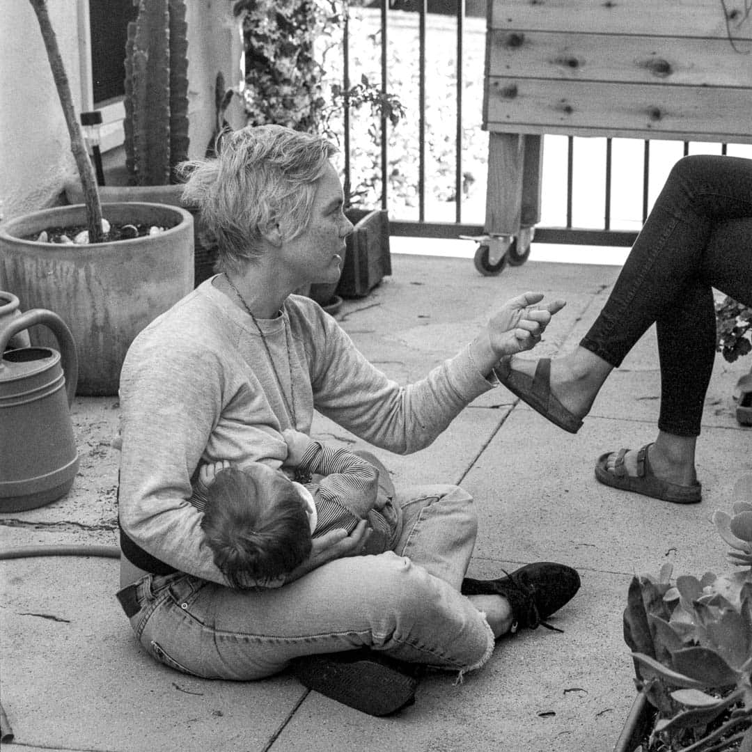 A woman seated in the garden with a baby asleep on her lap