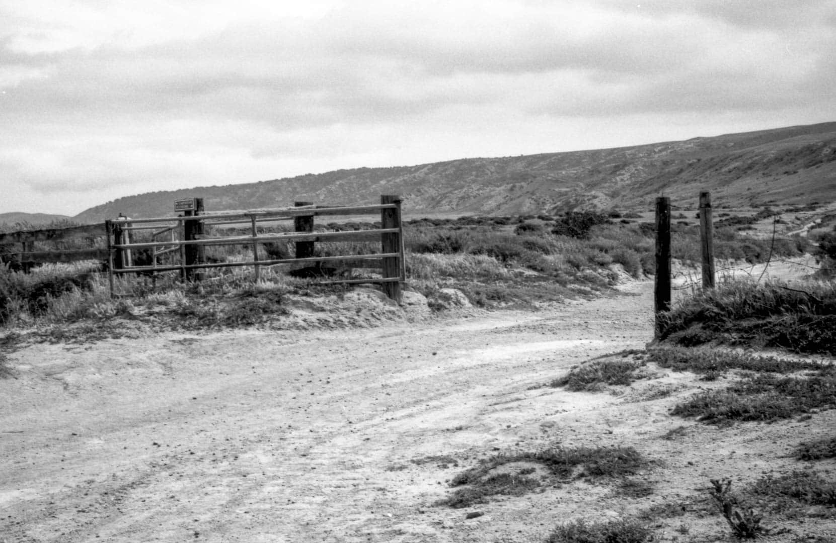 A metal gate on a wooden fence along a dirt path